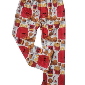 Puede incluir: Pantalones rojos y blancos con un patrón de dibujos animados de comida rápida, incluyendo patatas fritas, nuggets y una bebida. El texto "BBQ" aparece en el patrón.