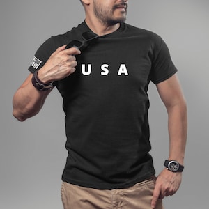 May include: A black t-shirt with a white "USA" graphic on the front. The shirt has a small American flag patch on the left sleeve.