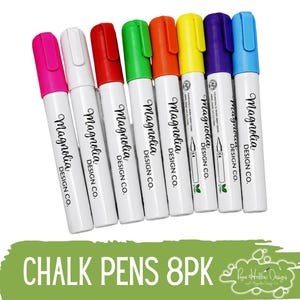 May include: A set of eight chalk pens with white barrels and colorful caps in pink, white, red, green, orange, yellow, purple, and blue. Each pen features the text Magnolia Design Co. printed in black. The text CHALK PENS 8PK is visible below.