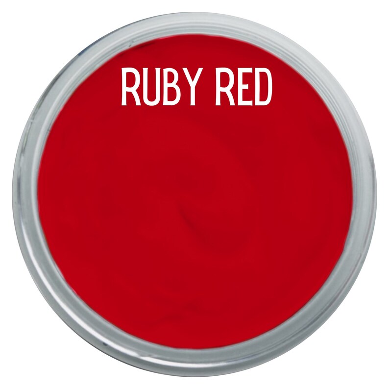 May include: A circular container filled with vibrant ruby red pigment or paint. The container features a clear, transparent rim and a smooth, solid red surface. The text "RUBY RED" is printed in a clean, white, sans-serif font across the top.