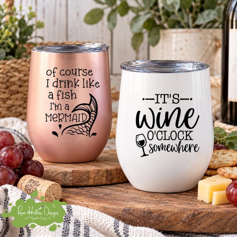 K&ouml;nnte beinhalten: Zwei stiellose Edelstahlbecher mit Deckeln. Der ros&eacute;goldene Becher tr&auml;gt den schwarzen Schriftzug of course I drink like a fish I'm a MERMAID mit einer Meerjungfrauenflosse. Der wei&szlig;e Becher tr&auml;gt den schwarzen Schriftzug IT'S wine O'CLOCK somewhere mit einem Weinglas-Symbol.
