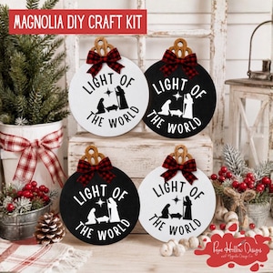 May include: Four circular wooden ornaments featuring a nativity scene silhouette and the text LIGHT OF THE WORLD. Each ornament is topped with a wooden cutout hanger and a red and black plaid fabric bow. Two are white with black text, two are black with white text.