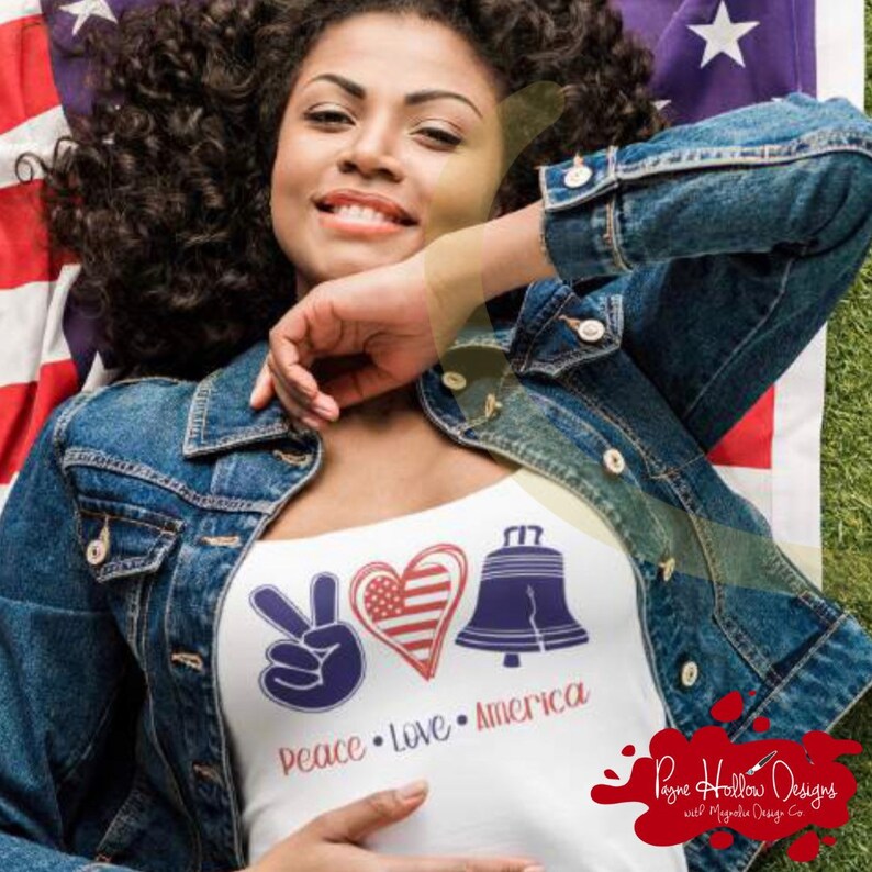 May include: A white tank top featuring a graphic print with a blue peace sign, a heart filled with the American flag pattern, and a blue Liberty Bell. Below the graphics, the text reads Peace, Love, and America in red and blue lettering.