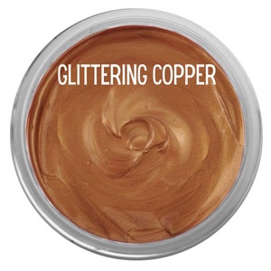 May include: A circular container filled with a thick, metallic copper-colored paste. The surface of the paste has a swirled texture and a shimmering finish. The text GLITTERING COPPER is printed in white capital letters across the top center.