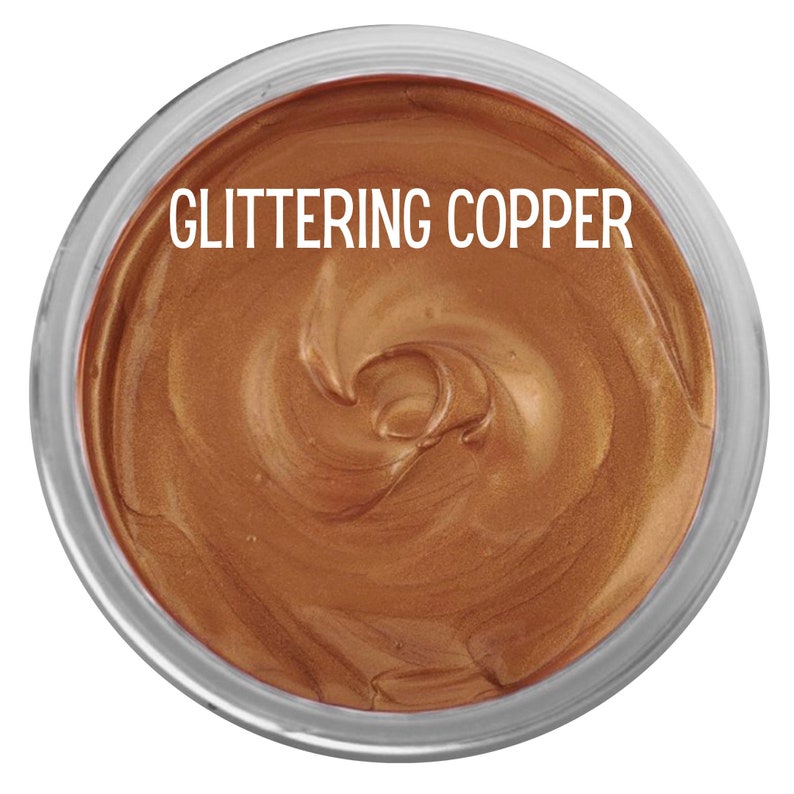 May include: A circular container filled with a thick, metallic copper-colored paste. The surface of the paste has a swirled texture and a shimmering finish. The text GLITTERING COPPER is printed in white capital letters across the top center.