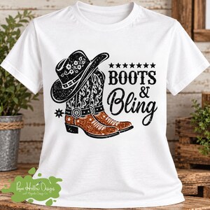 Peut inclure: Un t-shirt blanc &agrave; manches courtes avec une impression graphique repr&eacute;sentant un chapeau de cowboy noir et deux bottes de cowboy marron paillet&eacute;es. Le texte "BOOTS & BLING" est imprim&eacute; en noir &agrave; c&ocirc;t&eacute; des bottes, avec sept &eacute;toiles noires.