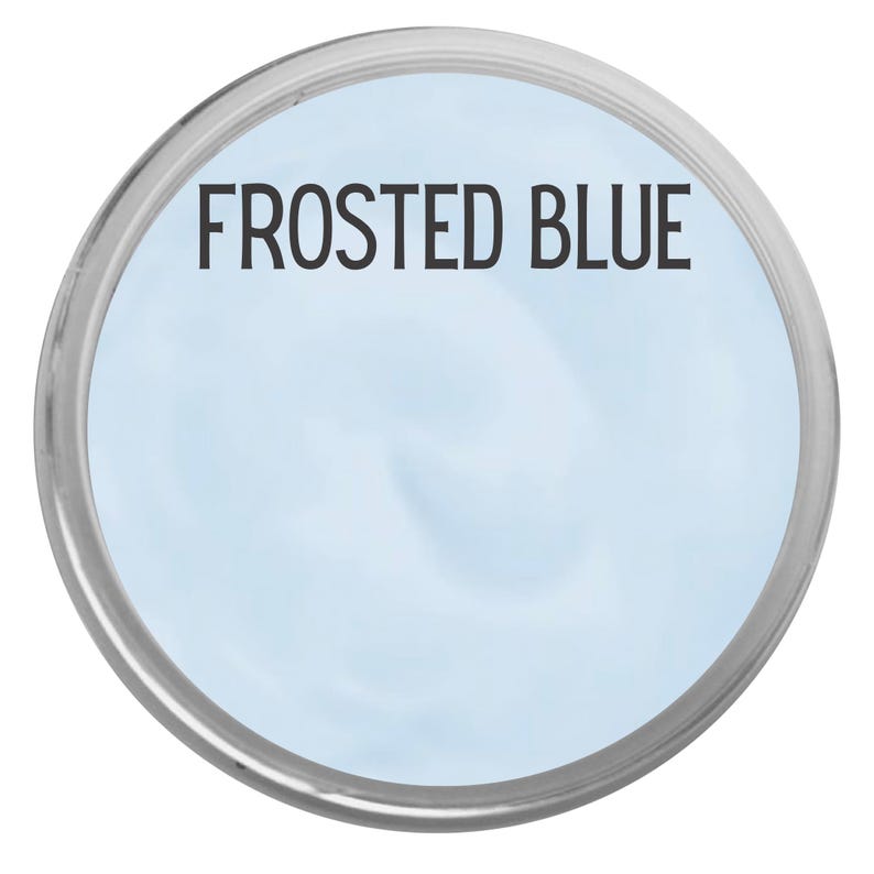May include: A round container with a silver rim, filled with a light blue substance. The text "FROSTED BLUE" is printed in black across the center of the container. The background is white.