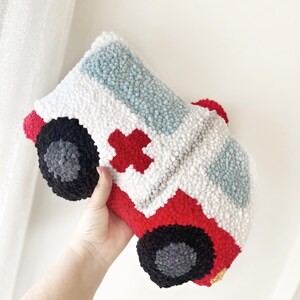 Puede incluir: Una almohada de ambulancia de felpa roja y blanca con una cruz roja en el lateral. La almohada est&aacute; hecha de hilo y tiene un efecto 3D.