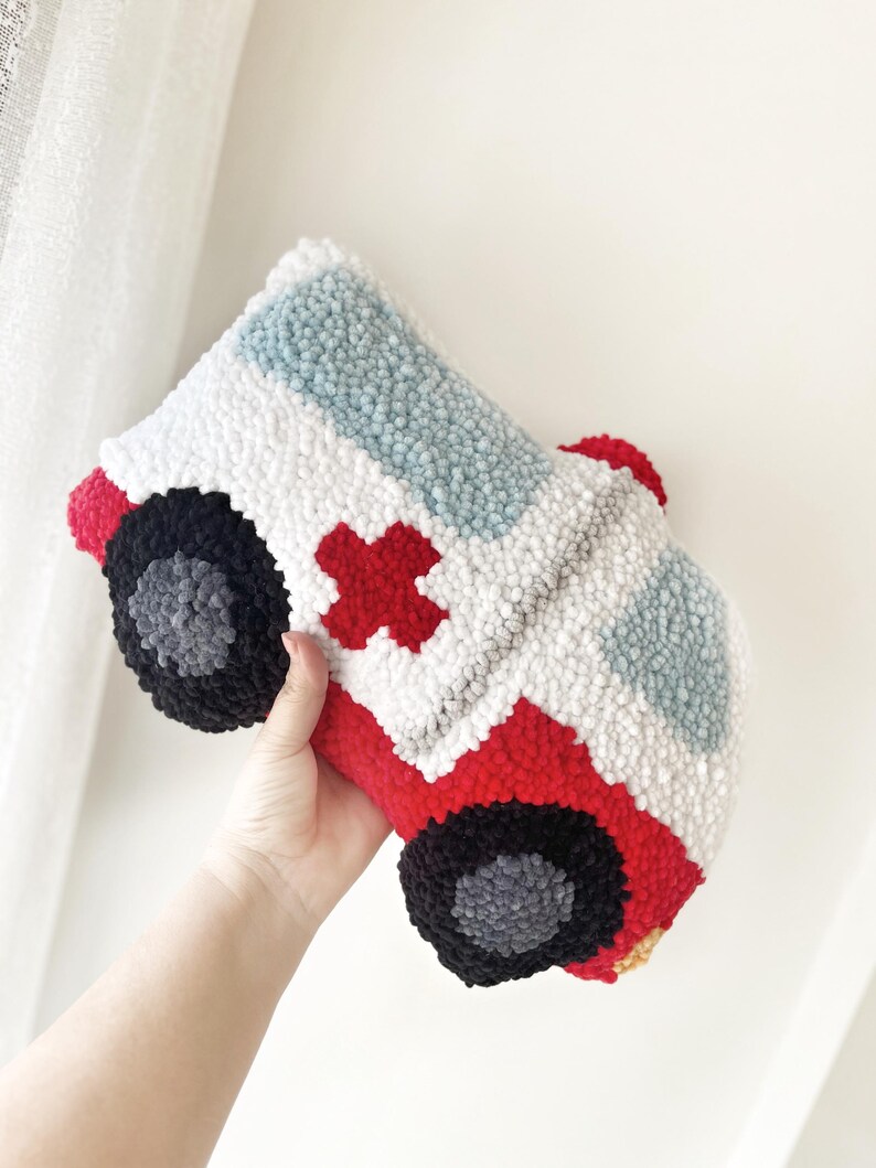 Puede incluir: Una almohada de ambulancia de felpa roja y blanca con una cruz roja en el lateral. La almohada est&aacute; hecha de hilo y tiene un efecto 3D.