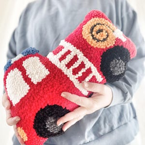 Puede incluir: Un juguete de peluche con forma de cami&oacute;n de bomberos rojo con detalles blancos y negros. El juguete est&aacute; hecho de hilo y tiene un efecto 3D.