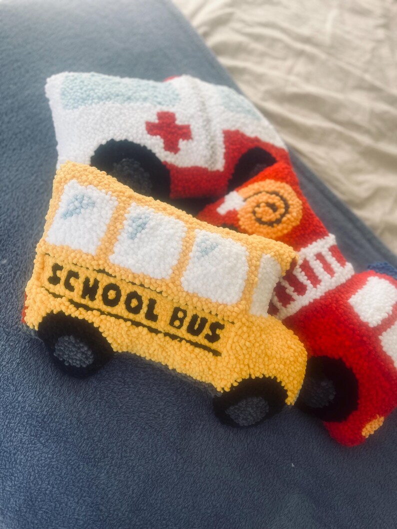 Puede incluir: Tres veh&iacute;culos de peluche: un autob&uacute;s escolar amarillo con las palabras "SCHOOL BUS" en el lateral, un cami&oacute;n de bomberos rojo con una cruz blanca en el lateral y una ambulancia blanca con una cruz roja en el lateral.