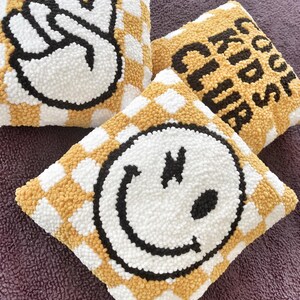 May include: Three square decorative pillows with a checkerboard pattern in yellow and white. One pillow features a peace sign, another says "Cool Kids Club", and the third has a smiley face. The designs are in black and white.