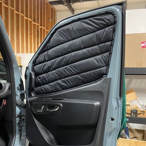 May include: Black quilted insulated window cover installed on a vehicle door. The cover is designed to fit the window frame and is made of a dark, possibly waterproof material. The door is light blue.