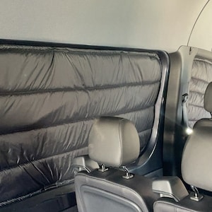 May include: Black quilted window coverings installed inside a vehicle. The coverings are rectangular and fit the shape of the windows. The interior of the vehicle includes black leather seats and a steering wheel.