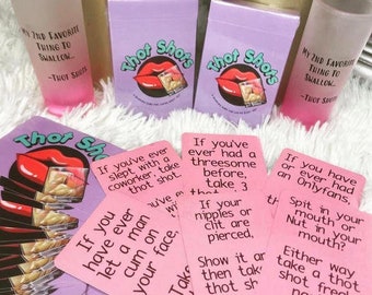 Puede incluir: Un juego de cartas rosa y morado llamado "Thot Shots" con una variedad de cartas que presentan frases sugestivas e instrucciones para tomar un shot. Las cartas están dispuestas sobre una superficie blanca y peluda con dos vasos de chupito rosas y dos cajas moradas con el nombre del juego.