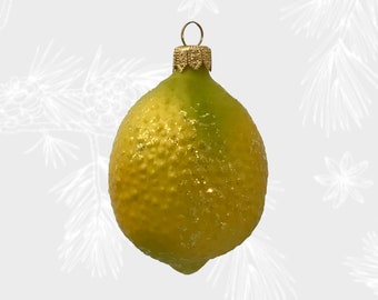 Op de afbeelding: Een gele en groene glazen kerstbal in de vorm van een citroen met een gouden top. De kerstbal heeft een glinsterende afwerking.
