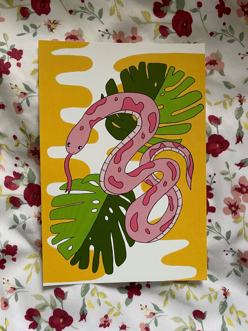 May include: A colorful art print featuring a pink snake with dark pink spots, a forked tongue, and a green leaf design. The background is yellow with white wavy shapes. The art print is on a white background.