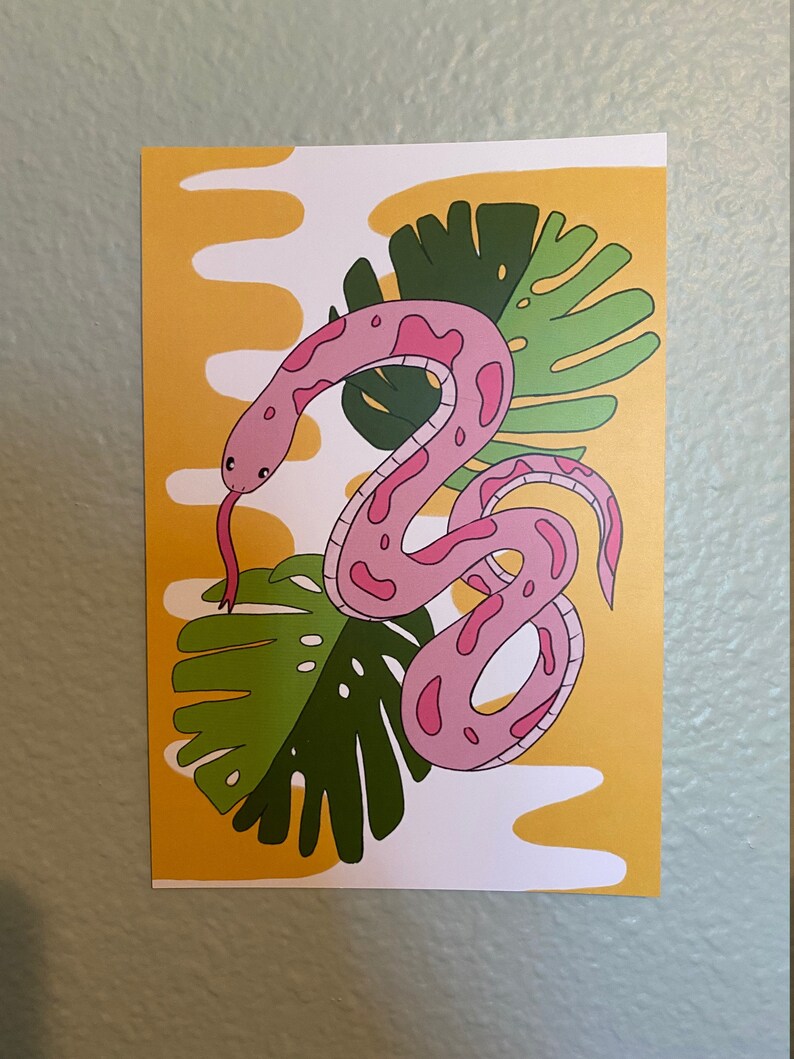 May include: A pink snake illustration with dark pink spots and a red tongue, set against a yellow and white background with green tropical leaves. The artwork has a playful, cartoonish style.