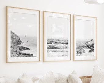 May include: A white couch with multiple pillows sits in a living room with a coffee table and a woven rug. Three black and white framed photos of seascapes hang on the wall behind the couch.