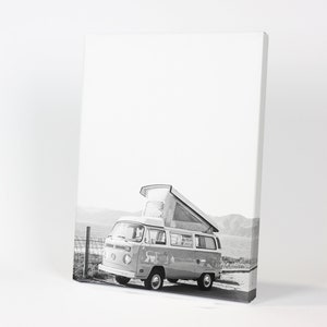 May include: Black and white photograph of a vintage Volkswagen camper van with a pop-up roof parked on a beach.