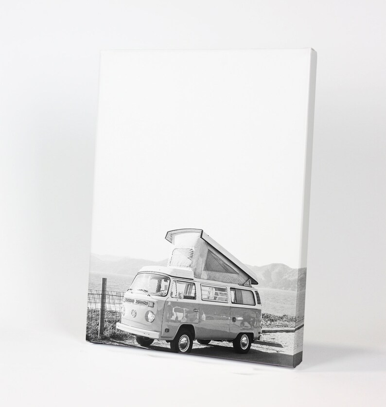 May include: Black and white photograph of a vintage Volkswagen camper van with a pop-up roof parked on a beach.