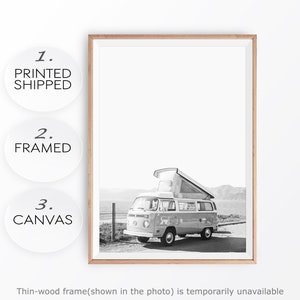 May include: Black and white photograph of a vintage camper van parked on a beach. The van has a pop-up roof and is facing the sea. The photo is framed in a thin wooden frame.