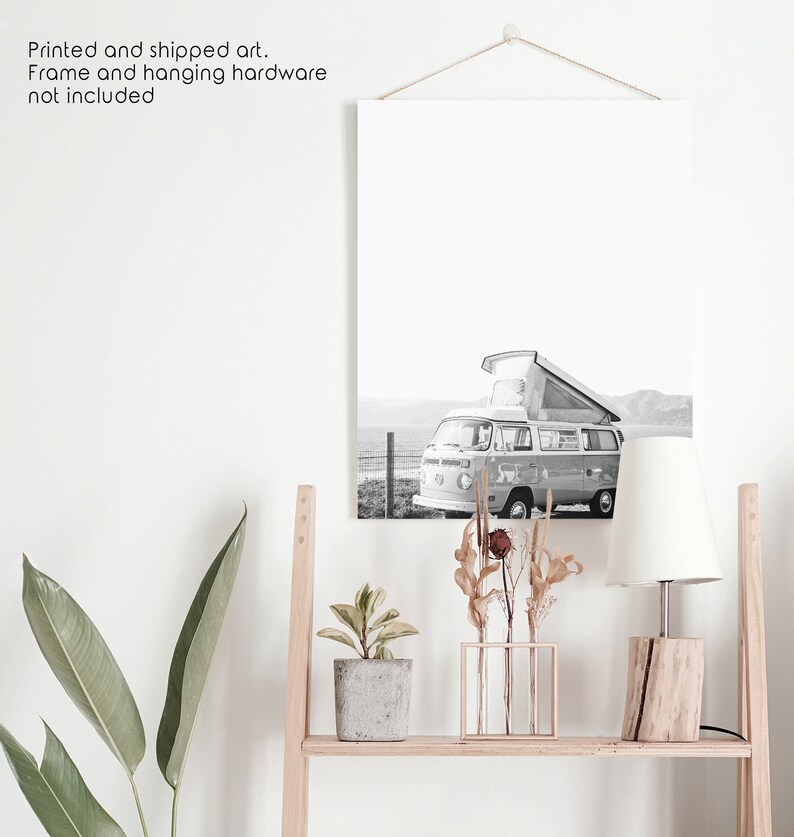 May include: Black and white photograph of a vintage camper van parked on a beach. The van has a pop-up roof and is facing the sea. The photo is printed on canvas and framed.