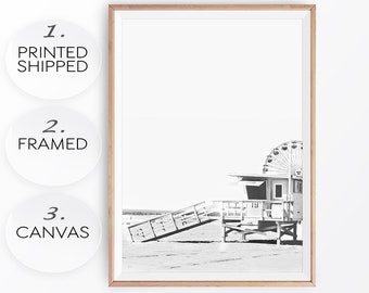 May include: Black and white photograph of a lifeguard stand on a beach with a Ferris wheel in the background. The lifeguard stand has a ladder and a sign that says "19".