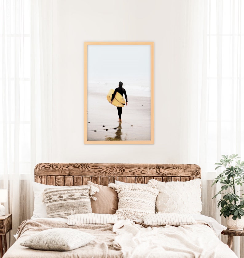 Puede incluir: Una fotograf&iacute;a enmarcada de una persona caminando por una playa con una tabla de surf. La persona lleva un traje de neopreno y lleva la tabla de surf sobre el hombro. La playa es arenosa y el agua es azul.