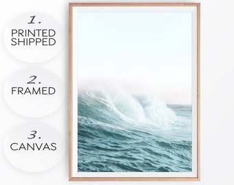 May include: A framed print of a large ocean wave crashing in the water. The wave is white and blue with a light blue background. The frame is a thin, light wood colour.