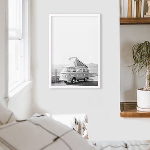 May include: Black and white photograph of a vintage camper van parked on a beach with a pop-up roof.
