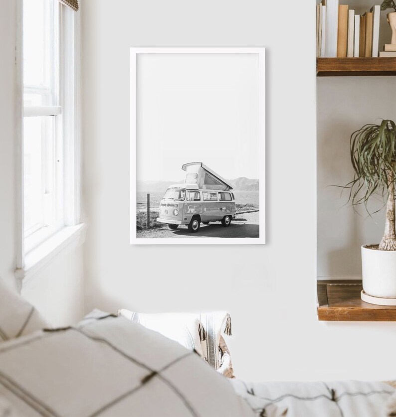 May include: Black and white photograph of a vintage camper van parked on a beach with a pop-up roof.