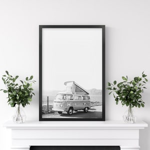 May include: Black and white photograph of a vintage camper van with a pop-up roof parked in a field. The van is facing the camera and the photo is framed in a black frame.