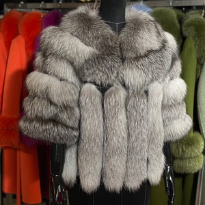 Puede incluir: Un chal de piel de zorro plateado con un cuello ancho y mangas largas. El chal se muestra en un maniqu&iacute; negro en una tienda.