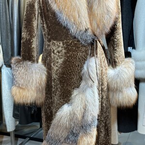 May include: A brown fur coat with a large fur collar and cuffs. The collar and cuffs are a lighter shade of brown than the coat. The coat is belted at the waist.
