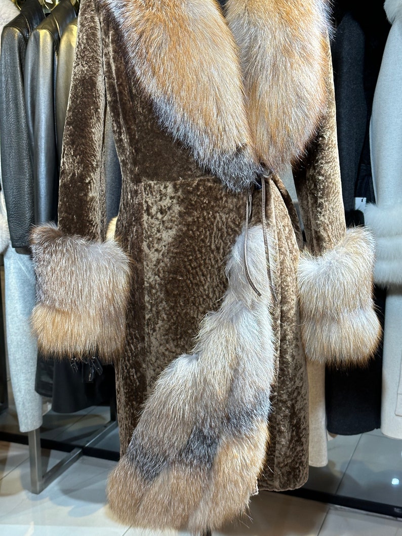 May include: A brown fur coat with a large fur collar and cuffs. The collar and cuffs are a lighter shade of brown than the coat. The coat is belted at the waist.