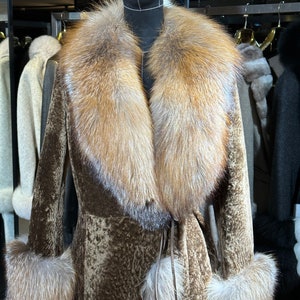 May include: A brown fur coat with a large fox fur collar and cuffs. The coat has a tie belt and is displayed on a mannequin.