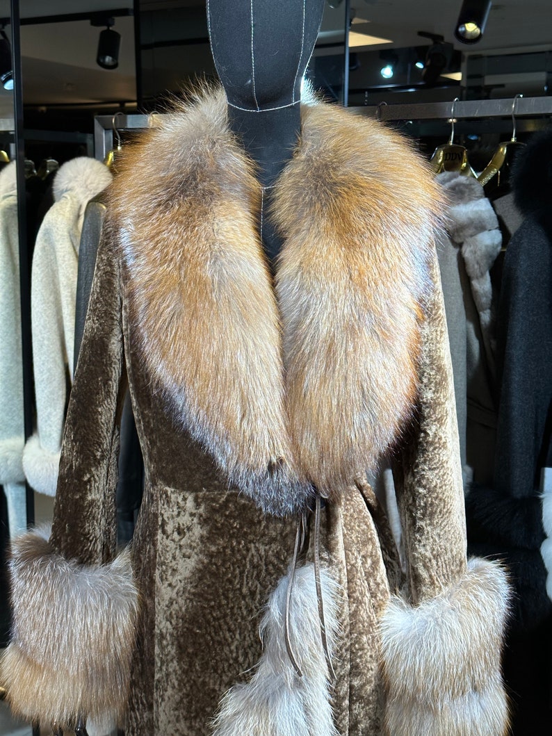 May include: A brown fur coat with a large fox fur collar and cuffs. The coat has a tie belt and is displayed on a mannequin.