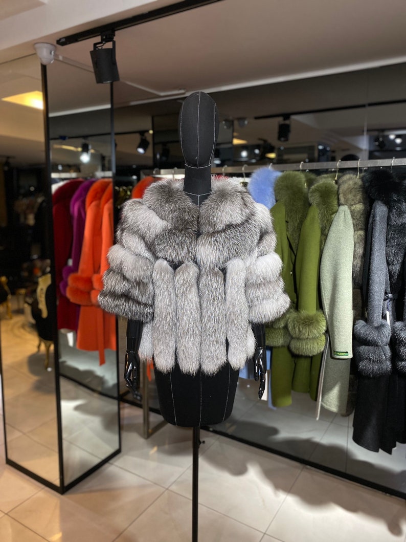 Puede incluir: Una estola de piel de zorro plateado con un dise&ntilde;o largo y fluido. La estola se exhibe en un maniqu&iacute; negro en un entorno de tienda minorista.