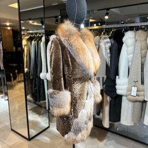 May include: A brown fur coat with a large fox fur collar and cuffs. The coat is on a mannequin in a store.