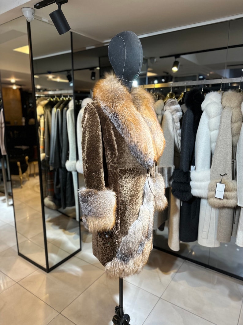 May include: A brown fur coat with a large fox fur collar and cuffs. The coat is on a mannequin in a store.