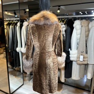 May include: A brown fur coat with a fox fur collar and cuffs. The coat is on a mannequin in a store.