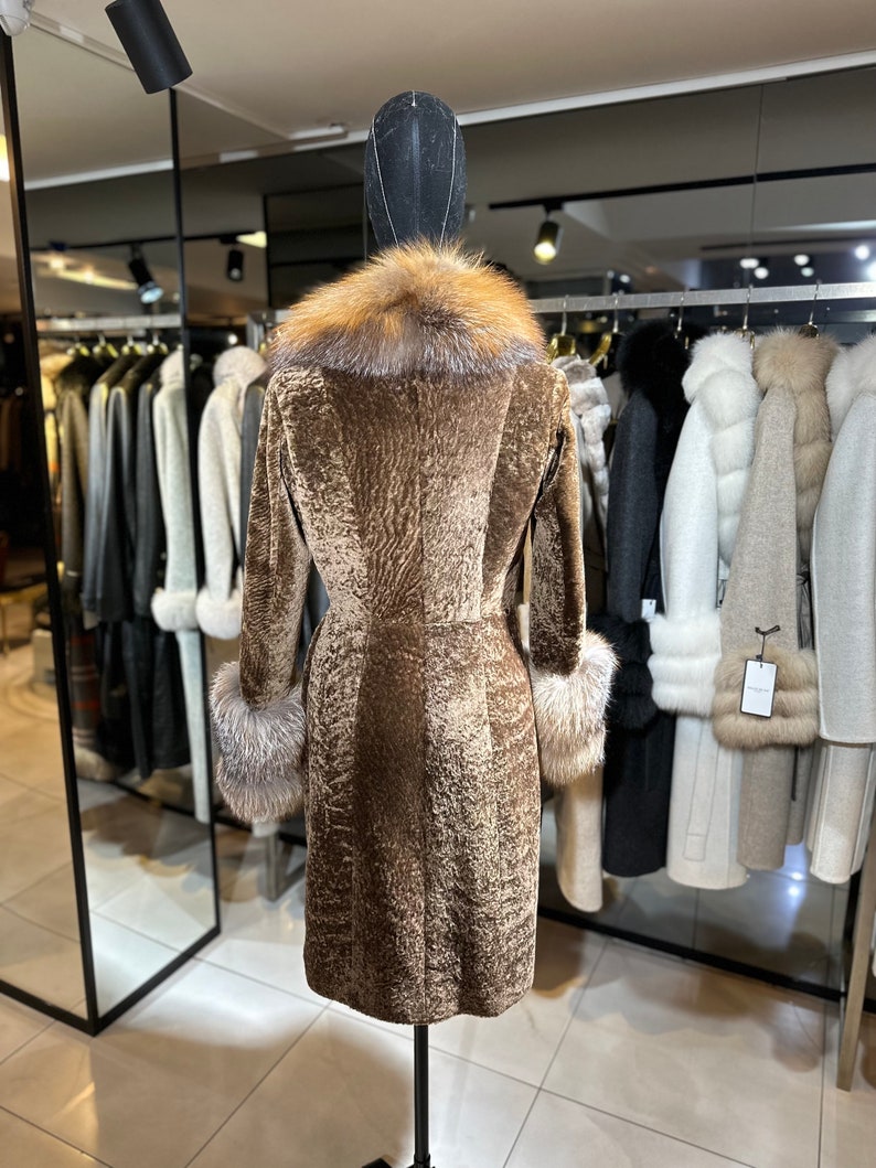 May include: A brown fur coat with a fox fur collar and cuffs. The coat is on a mannequin in a store.