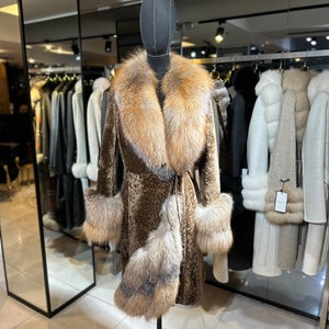 May include: A brown fur coat with a large fox fur collar and cuffs. The coat is on a mannequin in a store.