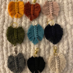Puede incluir: Nueve llaveros de macramé de colores con una variedad de colores que incluyen rosa, azul, verde, negro, blanco, gris, naranja y marrón. Los llaveros tienen todos la forma de una hoja.