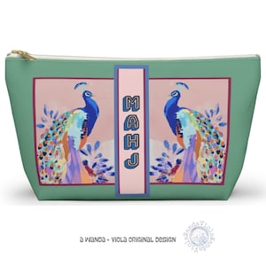 May include: A teal cosmetic bag with a gold zip. The bag features a pink rectangle with two peacock illustrations. The word "MAHJ" is vertically printed on a pink rectangle. The bottom of the bag has the text "a wanda + viola original design".