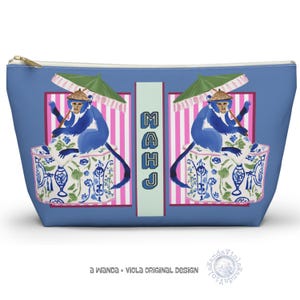 May include: Blue cosmetic bag with a gold zipper. The bag features a whimsical design of two blue monkeys holding parasols, seated in decorative cups against a pink and white striped background. The word "MAHJ" is vertically printed in the center.