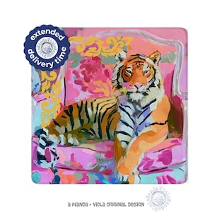 May include: A square art print featuring an oil painting of an orange and black tiger resting on a pink floral armchair with yellow scrollwork accents. The text "a WANDA + VIOLA ORIGINAL DESIGN" appears at the bottom, and a blue circular badge reads "extended delivery time".