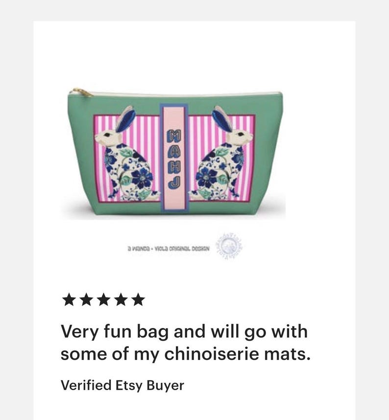 May include: A teal cosmetic bag with a gold zipper and a rectangular design featuring two rabbits with blue and white floral patterns. The bag has a pink and white striped center panel with the letters "MAHJ".