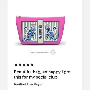 Puede incluir: Bolsa de cosm&eacute;ticos rosa con cremallera dorada, con dos dise&ntilde;os de leopardo azul. La bolsa tiene forma rectangular con un borde a rayas blanco y verde. El texto "MAHJ" se muestra en la bolsa.
